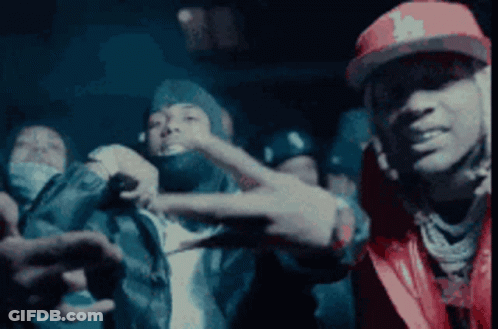 A Man In A Red Hat Is Making A Peace Sign In Front Of A Group Of People . GIF