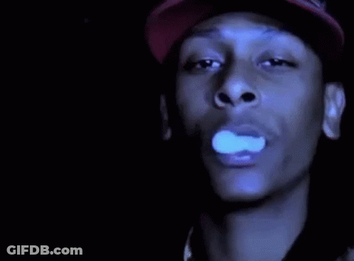 A Man In A Red Hat Is Smoking A Cigarette In The Dark . GIF
