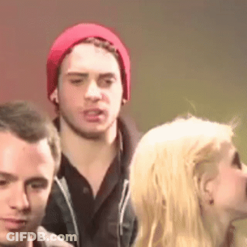A Man In A Red Hat Is Standing Next To A Woman In A Crowd . GIF