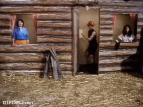 A Man In A Red Hat Stands In A Log Cabin GIF