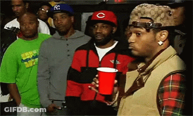 A Man In A Red Hat With The Letter C On It Holds A Red Cup In His Hand GIF