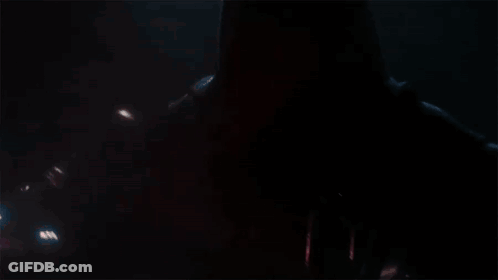 A Man In A Red Helmet Is Holding A Red Light Saber In The Dark . GIF