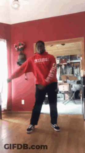 A Man In A Red Hoodie Is Dancing In A Living Room With A Red Wall GIF