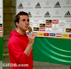 A Man In A Red Hoodie Is Eating An Ice Cream Cone In Front Of An Adidas Wall GIF