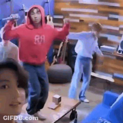 A Man In A Red Hoodie Is Holding A Microphone And Dancing In A Living Room . GIF
