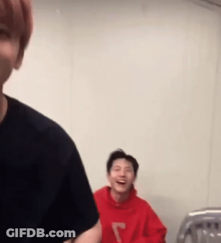 A Man In A Red Hoodie Is Laughing While Another Man In A Black Shirt Looks On . GIF