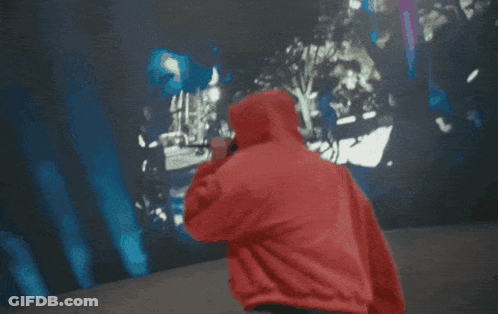 A Man In A Red Hoodie Is Singing Into A Microphone In Front Of A Crowd GIF