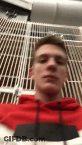 A Man In A Red Hoodie Is Taking A Selfie In Front Of A Metal Fence . GIF