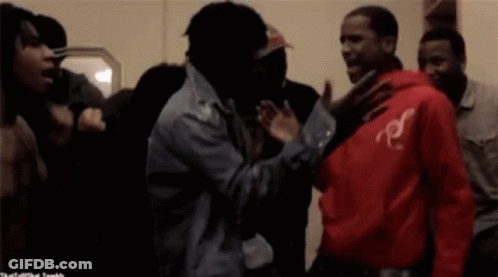 A Man In A Red Hoodie With The Letter R On It Stands In A Crowd Of People GIF