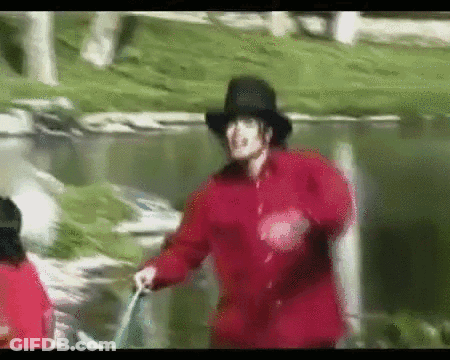 A Man In A Red Jacket And Black Hat Is Walking Across A Grassy Field GIF