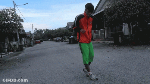 A Man In A Red Jacket And Green Shorts Is Walking Down The Street GIF