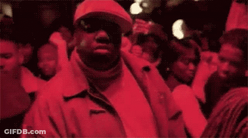 A Man In A Red Jacket And Hat Is Standing In A Crowd Of People GIF
