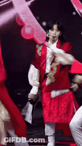 A Man In A Red Jacket And White Pants Is Dancing On A Stage GIF