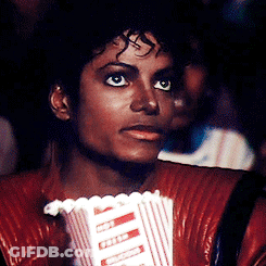 A Man In A Red Jacket Holds A Popcorn Bucket GIF