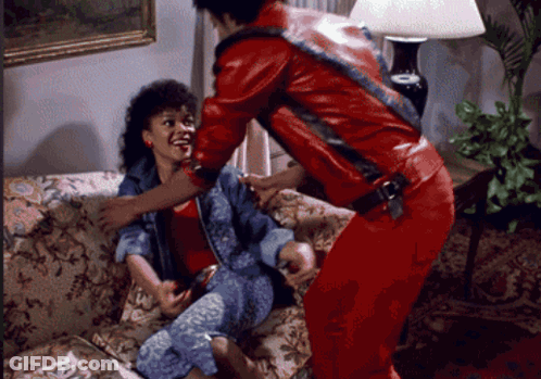 A Man In A Red Jacket Holds A Woman On A Couch GIF