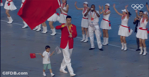A Man In A Red Jacket Is Carrying A Red Flag And A Boy In A White Shirt Is Holding A Flag GIF