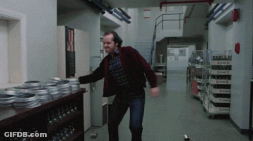 A Man In A Red Jacket Is Dancing In A Hallway With A Shelf Full Of Reels Of Film GIF