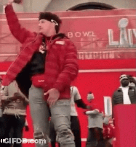 A Man In A Red Jacket Is Dancing In Front Of A Crowd At A Bowl . GIF