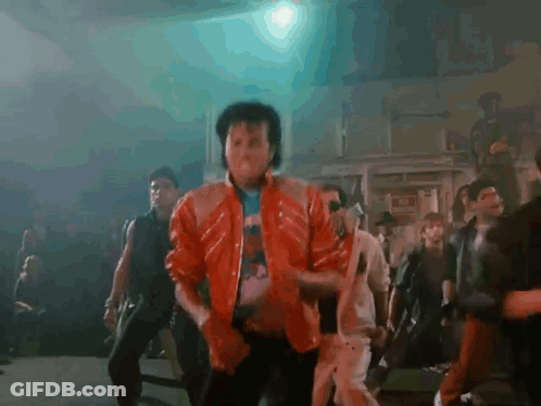 A Man In A Red Jacket Is Dancing In Front Of A Crowd In A Dark Room . GIF
