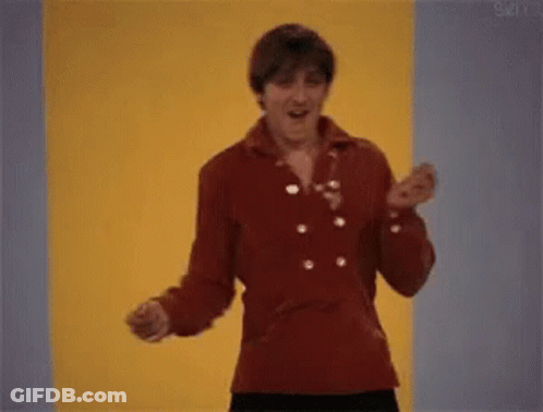 A Man In A Red Jacket Is Dancing In Front Of A Yellow Wall . GIF