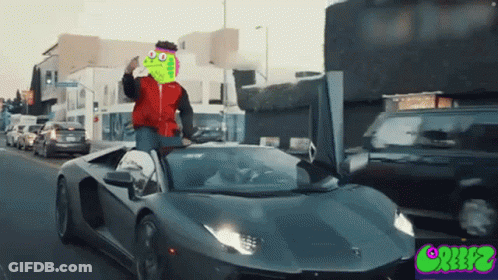 A Man In A Red Jacket Is Driving A Lamborghini With A Frog Face On The Hood GIF