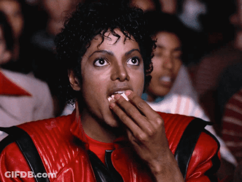 A Man In A Red Jacket Is Eating Popcorn While Watching A Movie GIF