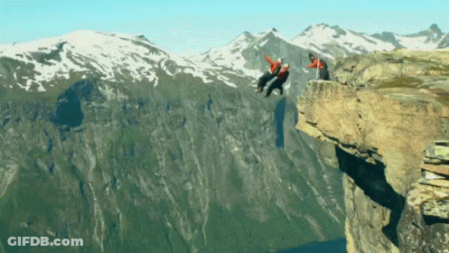 A Man In A Red Jacket Is Hanging Off A Cliff GIF