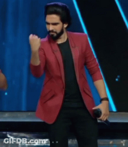A Man In A Red Jacket Is Holding A Microphone And His Fist In The Air GIF
