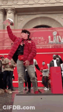 A Man In A Red Jacket Is Holding A Trophy In His Hand . GIF