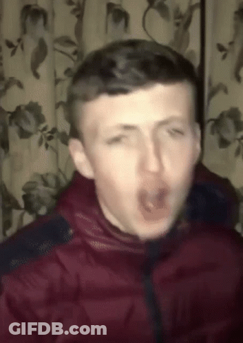 A Man In A Red Jacket Is Making A Funny Face In Front Of A Curtain With Flowers On It GIF