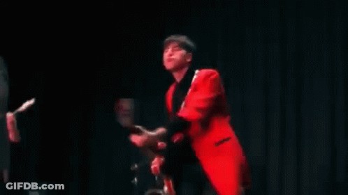 A Man In A Red Jacket Is Playing A Guitar In A Band . GIF