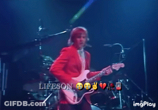 A Man In A Red Jacket Is Playing A Guitar On A Stage With The Words Lifeson On The Bottom Right GIF