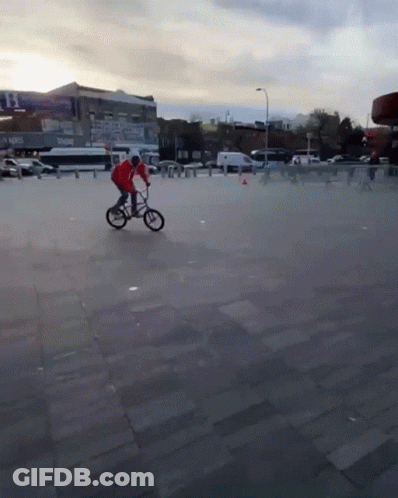 A Man In A Red Jacket Is Riding A Bike On A Concrete Pavement GIF