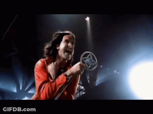 A Man In A Red Jacket Is Singing Into A Microphone On A Stage GIF
