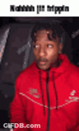 A Man In A Red Jacket Is Sitting In A Car And Looking At The Camera . GIF