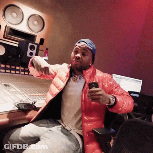 A Man In A Red Jacket Is Sitting In Front Of A Computer And Looking At His Phone GIF