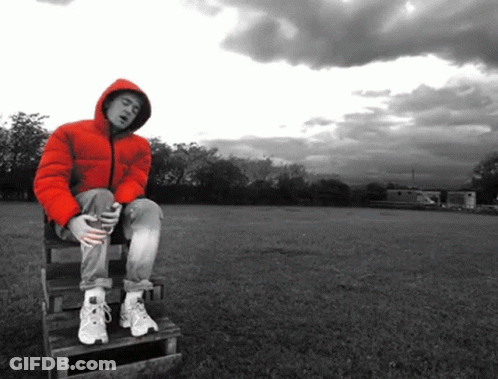 A Man In A Red Jacket Is Sitting On A Wooden Bench In A Field GIF