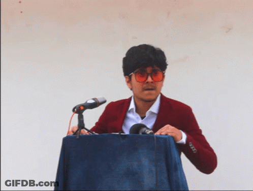 A Man In A Red Jacket Is Standing At A Podium With A Microphone GIF
