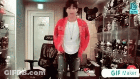 A Man In A Red Jacket Is Standing In A Room With A Chair . GIF