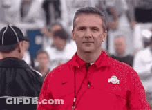 A Man In A Red Jacket Is Standing In A Stadium . GIF