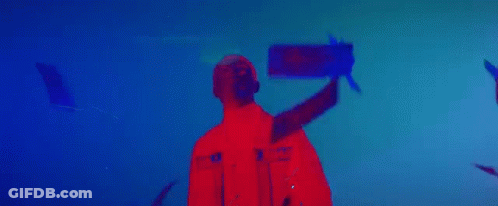 A Man In A Red Jacket Is Standing In Front Of A Blue Background In A Dark Room . GIF