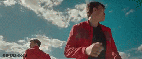 A Man In A Red Jacket Is Standing In Front Of A Blue Sky With Clouds . GIF