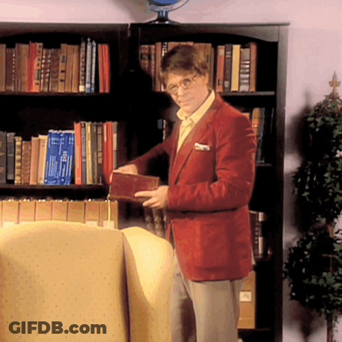 A Man In A Red Jacket Is Standing In Front Of A Bookshelf Holding A Book That Says ' I Love You ' GIF