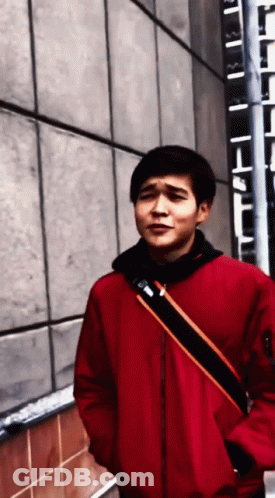 A Man In A Red Jacket Is Standing In Front Of A Building GIF