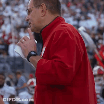 A Man In A Red Jacket Is Standing In Front Of A Crowd Holding A Piece Of Paper GIF