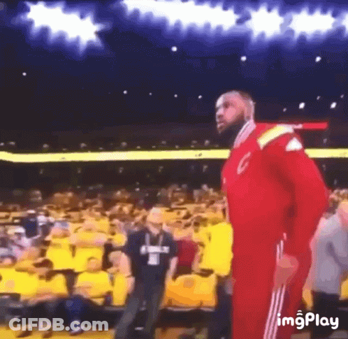 A Man In A Red Jacket Is Standing In Front Of A Crowd In A Stadium GIF