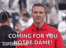 A Man In A Red Jacket Is Standing In Front Of A Crowd Of People . GIF