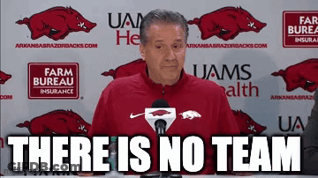 A Man In A Red Jacket Is Standing In Front Of A Microphone With The Words `` There Is No Team '' . GIF