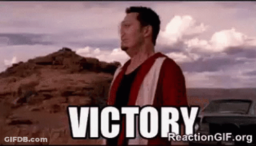 A Man In A Red Jacket Is Standing In Front Of A Mountain With The Word Victory Written On It . GIF