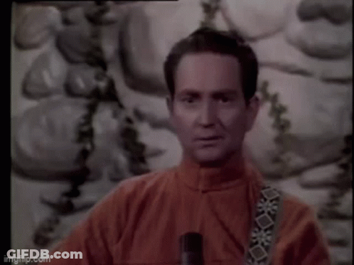 A Man In A Red Jacket Is Standing In Front Of A Painting And Holding A Microphone . GIF
